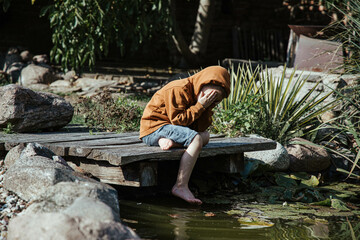 Smutne dziecko samotne na pomoście, drewniany pomost w starym ogrodzie, zagniewane, stęsknione, smutne