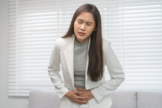 Flatulence, abdomen asian young business woman in suit at home, hand in stomach ache, expression face suffer from food poisoning, abdominal pain and colon problem, gastritis or diarrhoea, inflammation