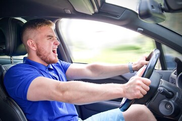 Handsome frightened fearful guy, driver, young scared man shocked about to have accident, driving car fast on road holding steering wheel of automobile. Unfastened by a seat belt. Traffic violation