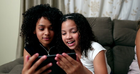 Two preteen girls reacting with excitement to entertainment media on cellphone screen