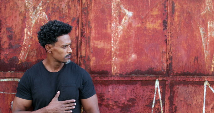 Serious African Man Standing Outside Surveilling Neighborhood Street Looking Sideways In Urban Environment