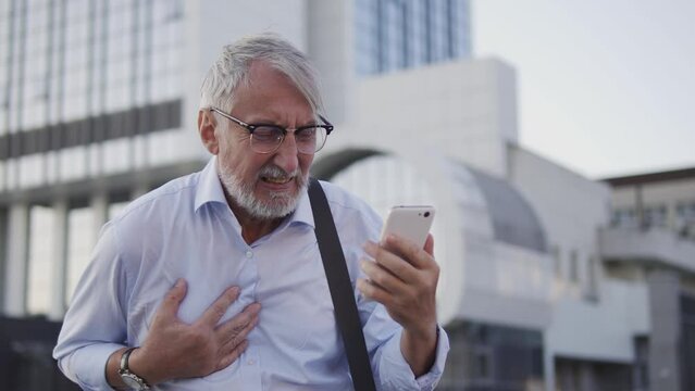 Old gray-haired businessman checking his banking account and suddenly feeling bad, risk of heart attack because of fraud, man lost all his money, falling stocks in the stock market, bankruptcy