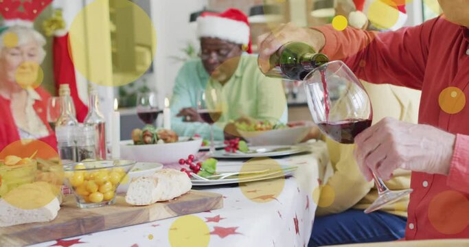 Animation of yellow light spots over caucasian senior man pouring wine at christmas dinner table