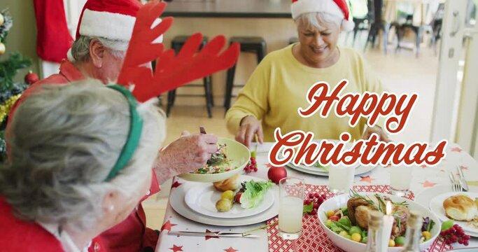 Animation of happy christmas text over diverse senior friends laughing at christmas dinner table