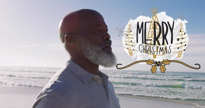 Animation of merry christmas text over happy senior african american man meditating on sunny beach