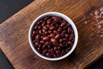 Black, canned beans in a white saucer against a dark concrete background