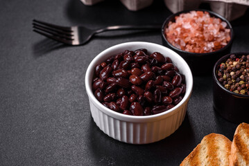 Black, canned beans in a white saucer against a dark concrete background