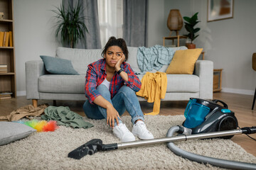 Unhappy tired young african american female sit on floor with vacuum cleaner, have problems with...
