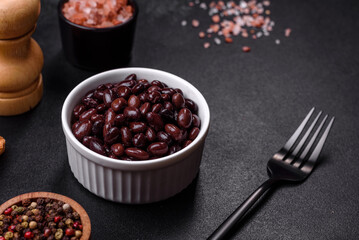 Black, canned beans in a white saucer against a dark concrete background