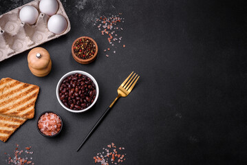 Black, canned beans in a white saucer against a dark concrete background