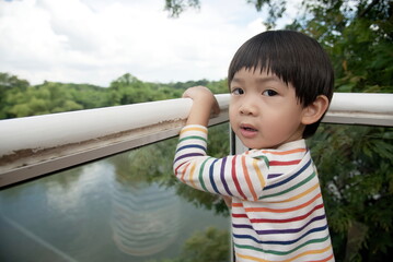 Little asian child standing at balcony bars and looking at camera in the morning