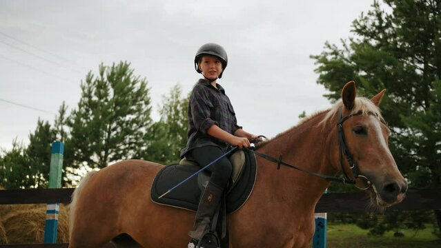 little girl is riding pony in sport equestrian club for children, schooler is resting in countryside