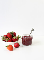 Homemade strawberry preserves or jam in a mason jar surrounded by fresh organic strawberries. Selective focus with blurred foreground and background.