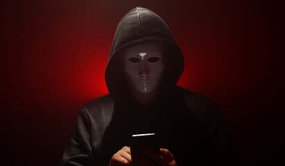 Man wearing mask with hoodie launches virus from smartphone.