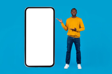 Cheerful black guy pointing at big cell phone, mockup