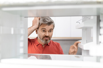 Overwhelmed middle aged man looking inside empty fridge