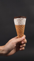 Hand is holding ice cream cone with black background.