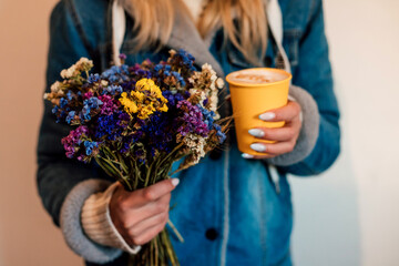 Bouquet of flowers and a glass of coffee in women's macro hands