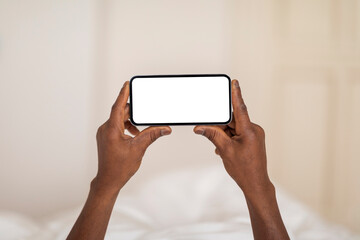 Mobile Mockup. Unrecognizable Black Man Holding Blank Smartphone While Lying In Bed