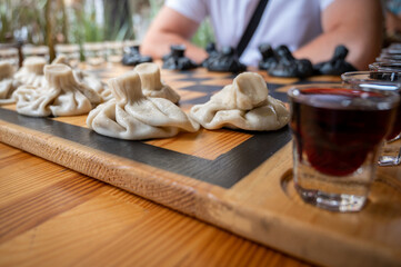 Traditional Georgian dish, khinkali Kalakuri, on wooden table, chess board, rustic, side view, black and light dough, playing chess. Selective focus, side view. Meat and cheese dishes