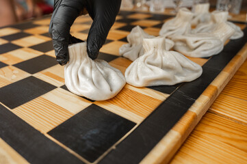 Traditional Georgian dish, khinkali Kalakuri, on wooden table, chess board, rustic, side view, black and light dough, playing chess. Selective focus, side view. Meat and cheese dishes