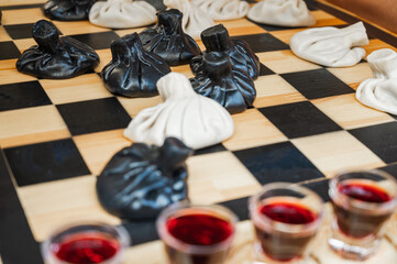 Traditional Georgian dish, khinkali Kalakuri, on wooden table, chess board, rustic, side view, black and light dough, playing chess. Selective focus, side view. Meat and cheese dishes