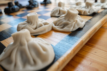 Traditional Georgian dish, khinkali Kalakuri, on wooden table, chess board, rustic, side view, black and light dough, chess game. Selective focus, side view. Meat and cheese dishes