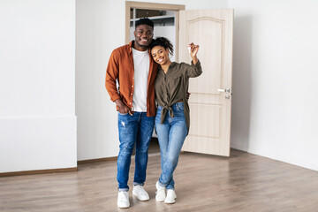 Contented Black Couple Showing Key Standing Hugging In New Apartment