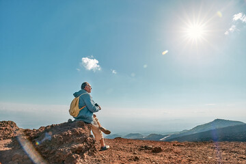 Rear view of man looking through binoculars at panoramic view of colorful summits of active volcano...