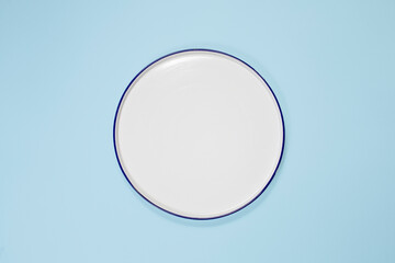 white plate in the center, top view, copy space. On a blue background - obrazy, fototapety, plakaty