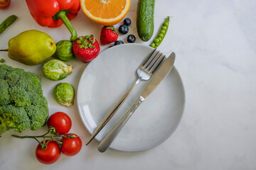 Plate fork knife vegetables and fruits on a light background