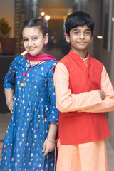 2 Indian kids, brother and sister friends siblings dressed up in ethnic wear smiling looking at the...