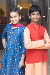 2 Indian kids, brother and sister friends siblings dressed up in ethnic wear smiling looking at the camera celebrating diwali Hindu festival Laxmi poojan with ambient light bokeh