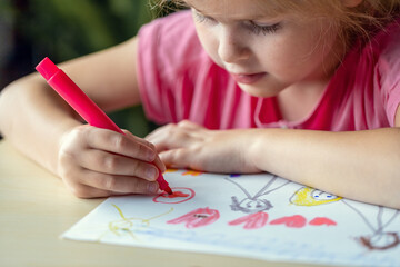 Child drawing a picture with colored markers. Little girl, sitting at the desk, learning to draw.