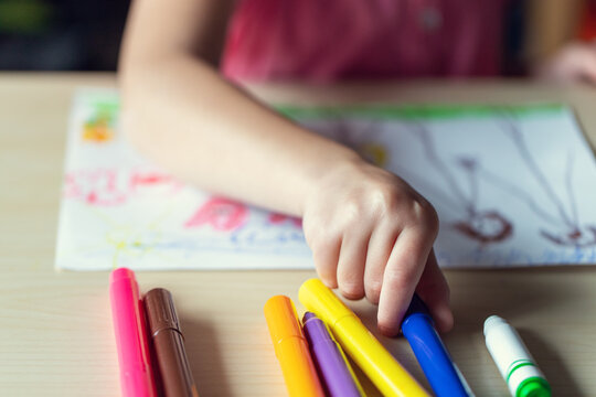 Hand of a child drawing a picture with colored markers. Little kid, sitting at the desk, learning to draw.