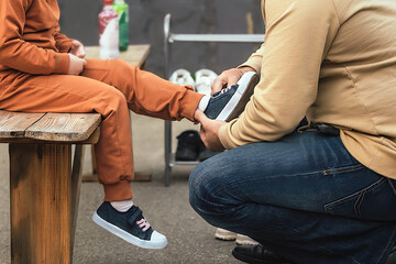 a man looks after and cares for his little daughter and helps her put on her sneakers in an outdoor park - obrazy, fototapety, plakaty