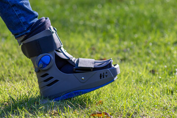 Boy with broken foot and orthopedic shoe or walker after bone fracture rests in public park on...