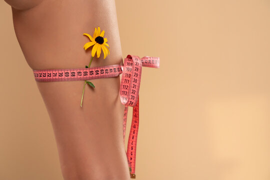 Woman measuring her thigh using a tape measure, isolated on beige background