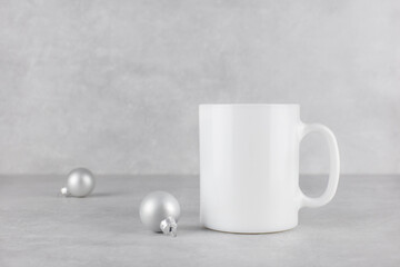 Blank white mug mockup with christmas silver balls on light concrete stone background. Holiday...