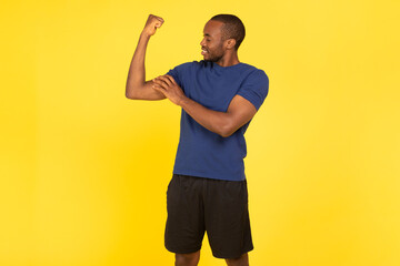 Fototapeta premium Sporty African American Guy Showing Biceps Muscles On Yellow Background