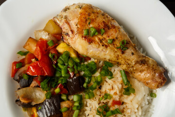 Rice with stewed vegetables in sauce and chicken leg in a white plate close-up.
