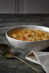 Homestyle chicken noodle soup in a white bowl with napkin and antique spoon on a green tabletop
