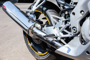 The rear wheel of a powerful sports bike with chrome tailpipe.