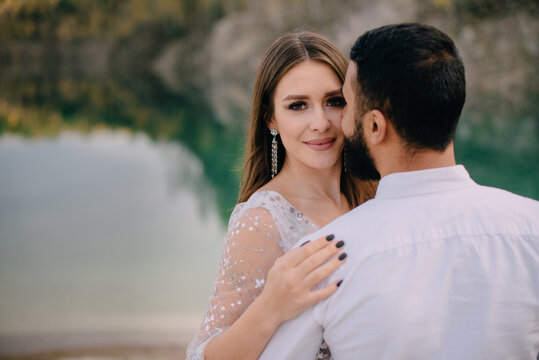 Interracial relations. Middle Eastern groom and Caucasian bride hug against a beautiful lake. A man kisses a woman on the cheek.