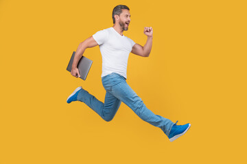 Fototapeta na wymiar man running with computer. man hold laptop isolated on yellow background. jumping man