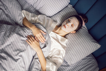 sexy brunette woman lies with her back on the bed in front of the bedroom window in a rejuvenating...