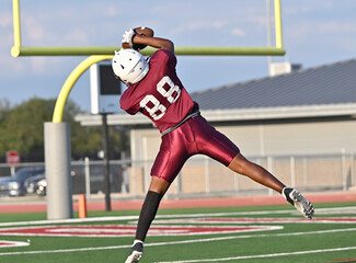 Young athletic tackle football player leaping high to make a catch during a game