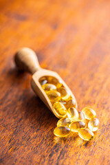 Fish oil capsules. Yellow omega 3 pills in wooden scoop on wooden table. - obrazy, fototapety, plakaty