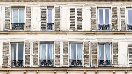 Fototapeta na wymiar Wood shutters with peeling paint flank windows with black wrought iron railings on a building in Paris France.