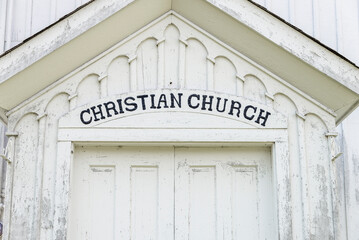 Close up of Christian Church sign above the doors to a white painted church.